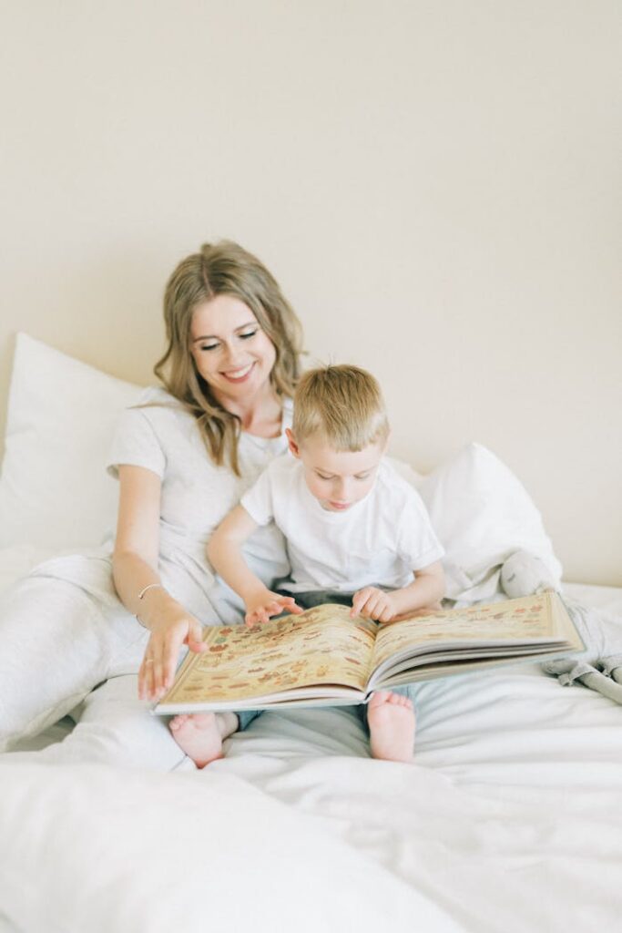 A mother and her young son enjoy reading a book together on a cozy bed indoors.