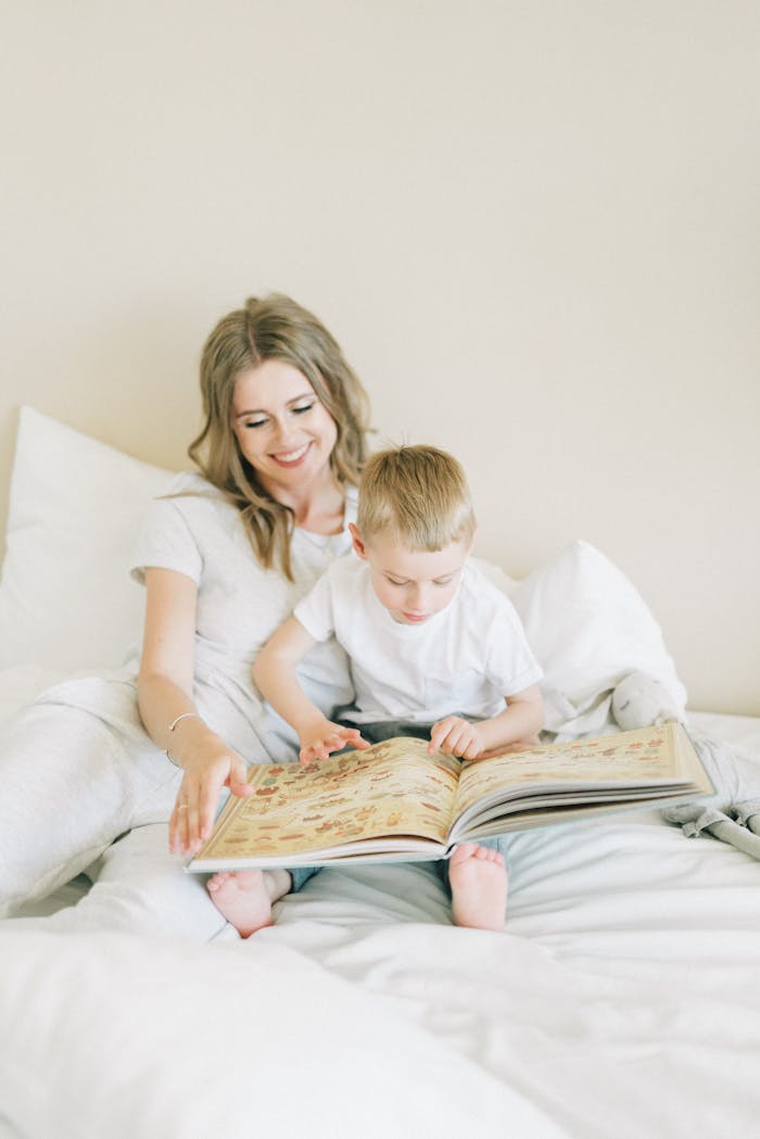 A mother and her young son enjoy reading a book together on a cozy bed indoors.