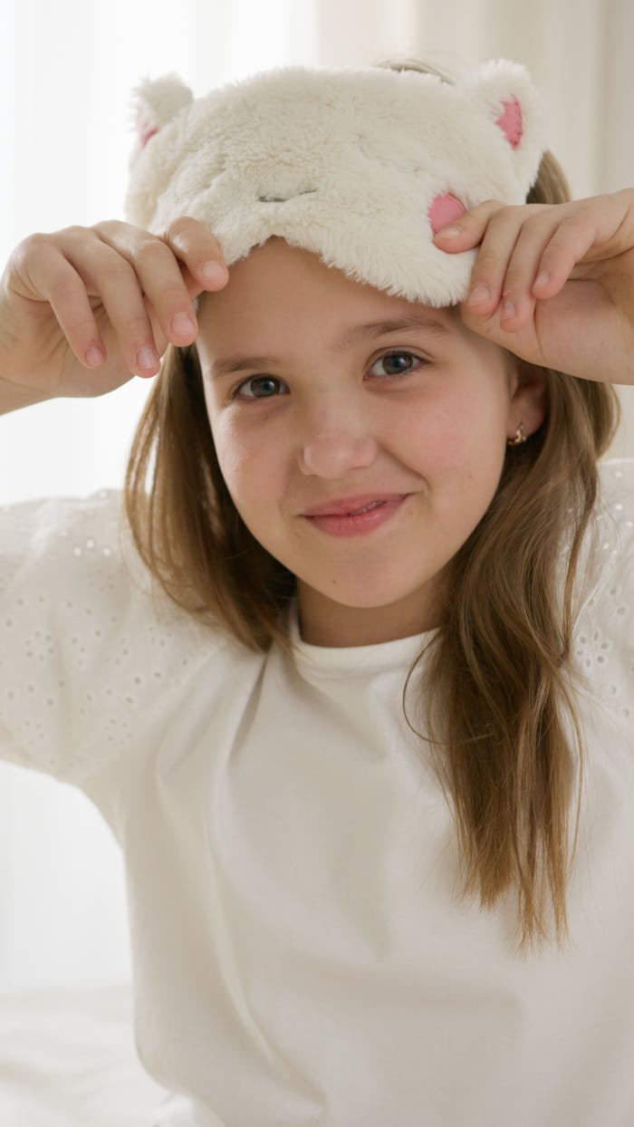 Charming girl adjusting her fluffy cat ear sleep mask indoors, embodying childhood innocence and joy.